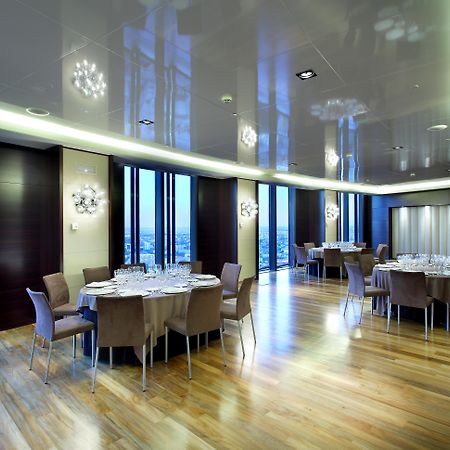 Eurostars Madrid Tower Hotel Exterior photo The photo depicts a modern dining room or banquet hall with large windows that provide a view of the outside. The room features elegant wooden flooring and contemporary furniture, including round tables set with plates, glasses, and cutlery. Various 