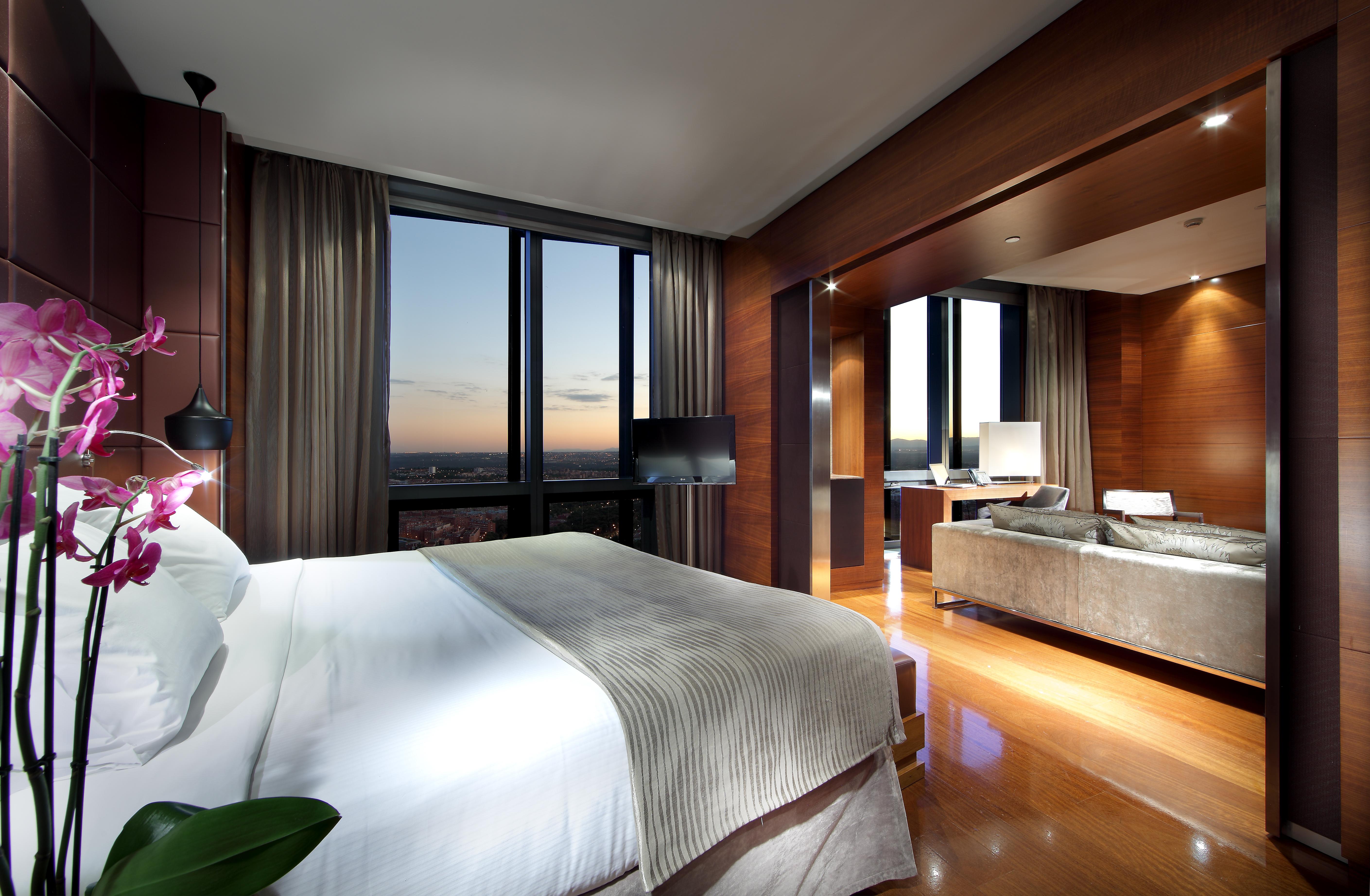 Eurostars Madrid Tower Hotel Exterior photo The photo depicts a modern hotel room interior. It features a spacious layout with a large bed dressed in white linens, accompanied by a subtle patterned blanket. To the side, there is a small decorative plant. 

The room is illuminated by ambient li