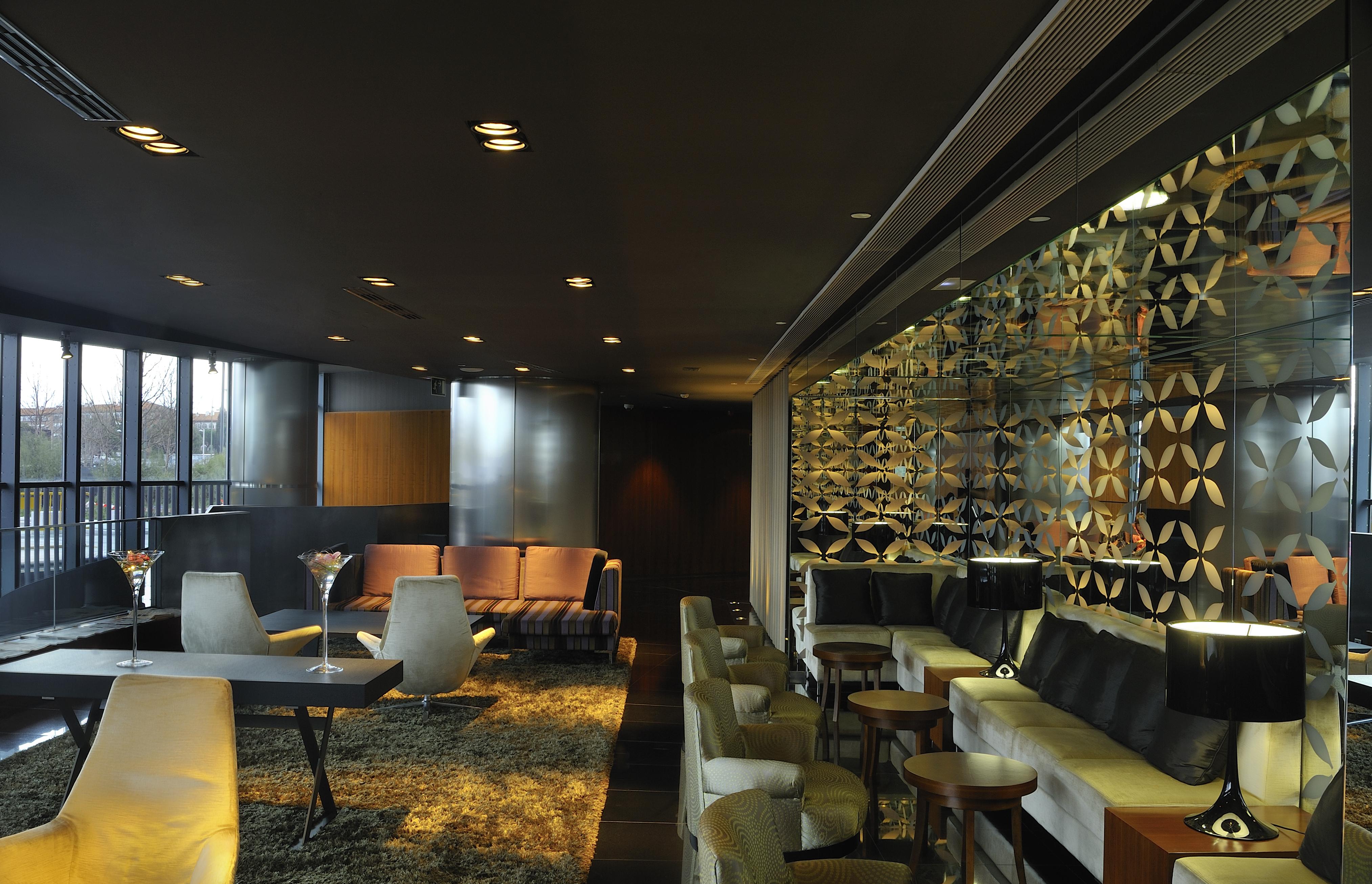 Eurostars Madrid Tower Hotel Exterior photo The photo shows a contemporary and stylish interior space, likely a lounge or bar. The design features a mix of seating arrangements, including plush chairs and modern sofas, set against a dark backdrop with soft lighting. A decorative wall with an i
