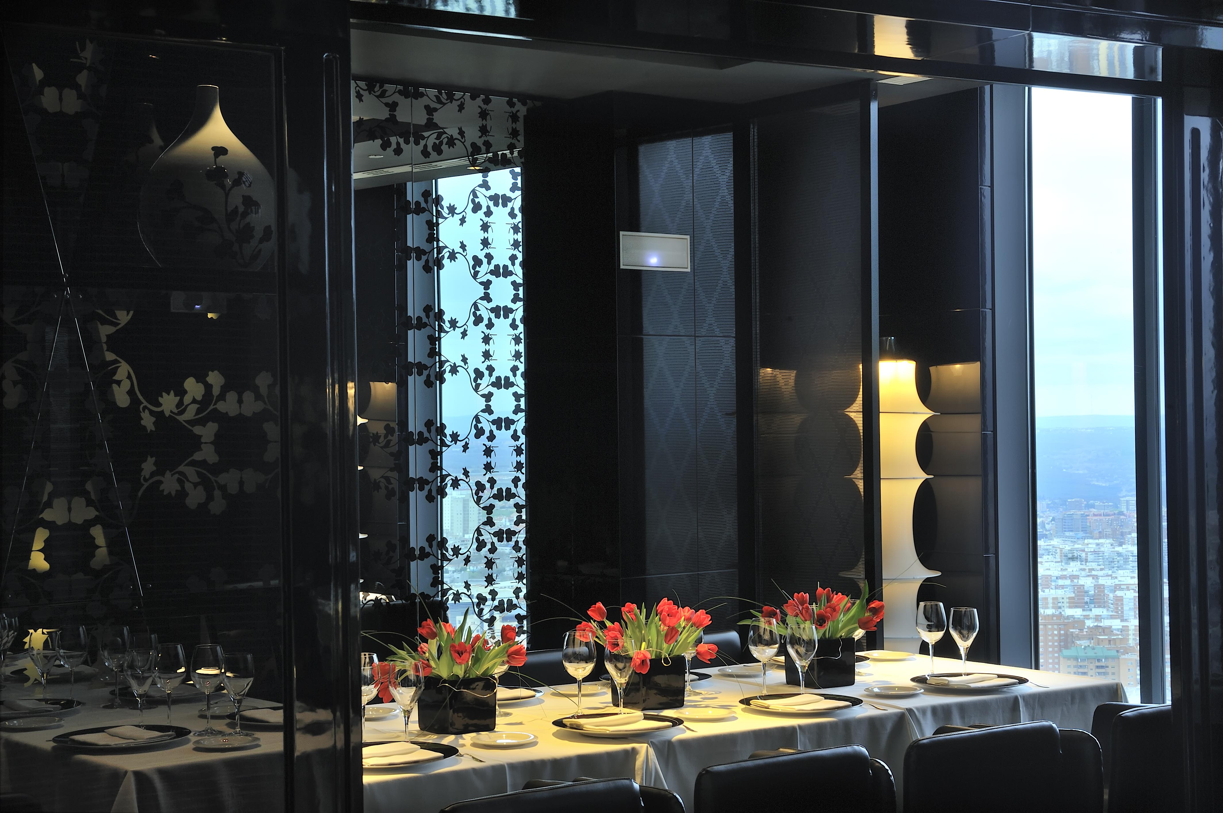 Eurostars Madrid Tower Hotel Exterior photo The photo shows a stylishly decorated dining area with a long table set for a meal. The table is adorned with elegant plates, glasses, and small vases of vibrant tulips as centerpieces. The interior design features a mix of dark and light elements, w