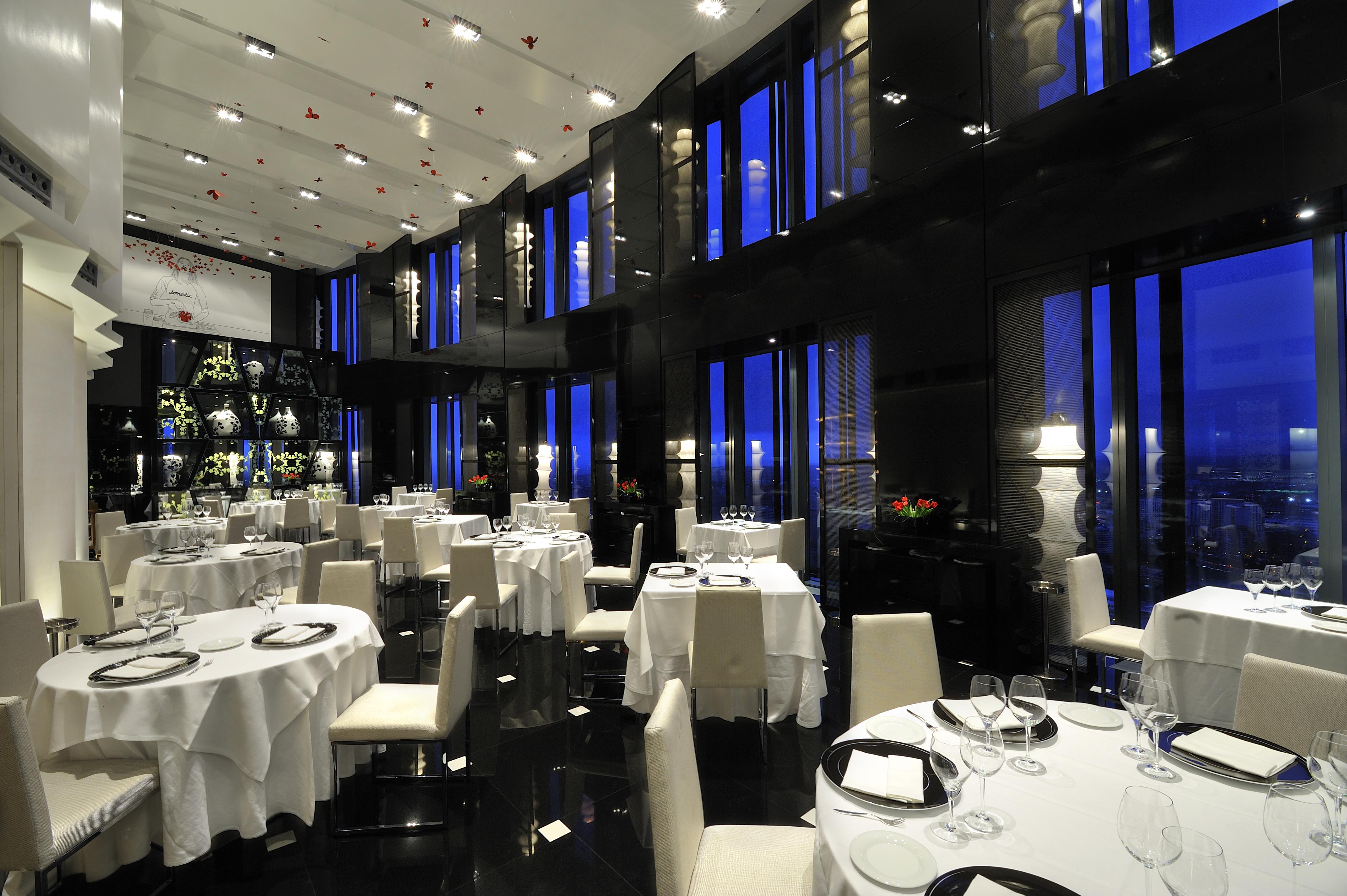 Eurostars Madrid Tower Hotel Exterior photo The photo shows an elegant restaurant interior, characterized by its modern design and luxurious ambiance. The space features several round dining tables, each set with white tablecloths and tableware, including wine glasses. The walls are made of da