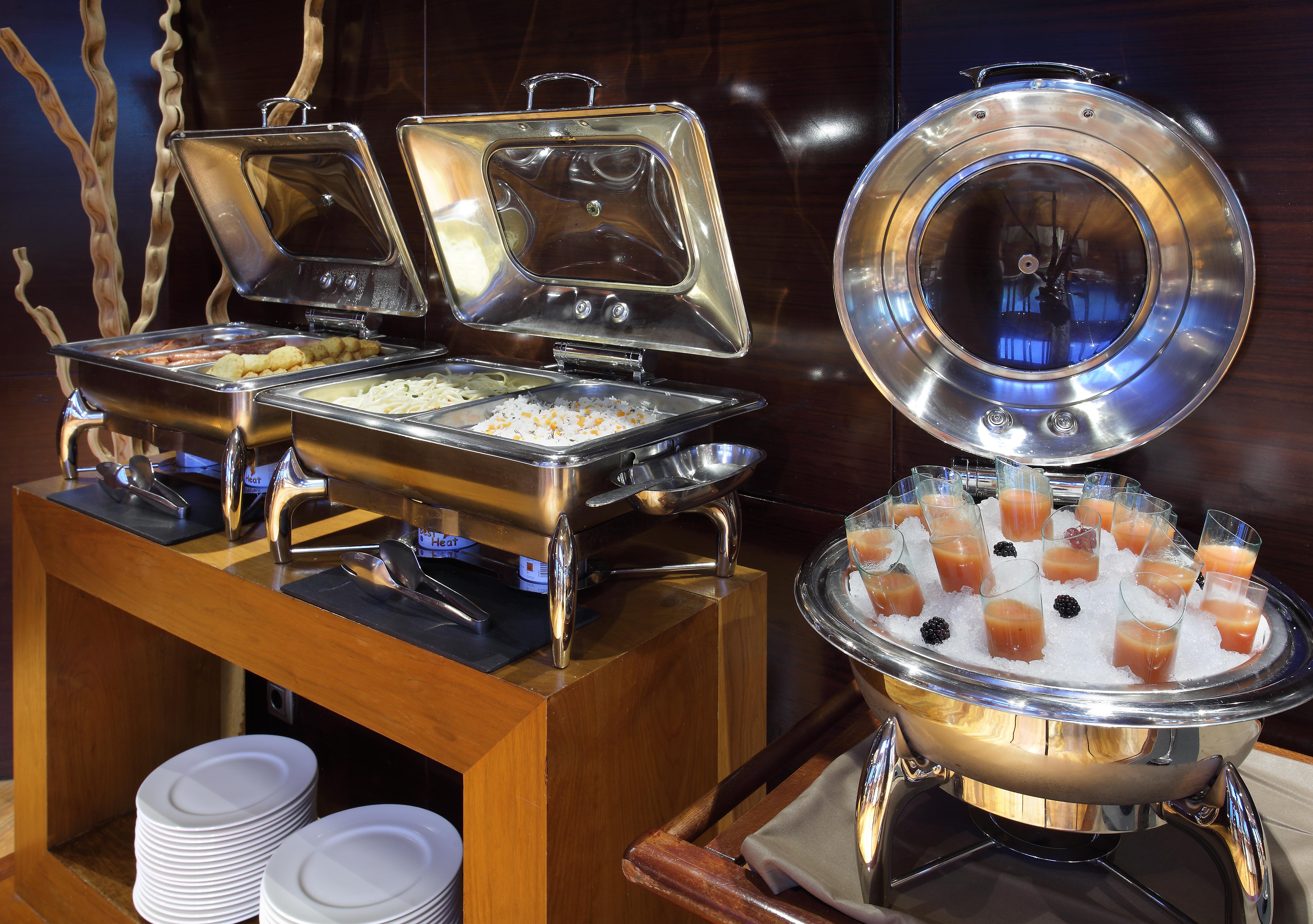 Eurostars Madrid Tower Hotel Exterior photo The photo shows a buffet setup with several food items. On the left, there are two stainless steel chafing dishes, each containing food, possibly rice or a similar dish. On the right, there is a round chafing dish that holds small cups or glasses fil