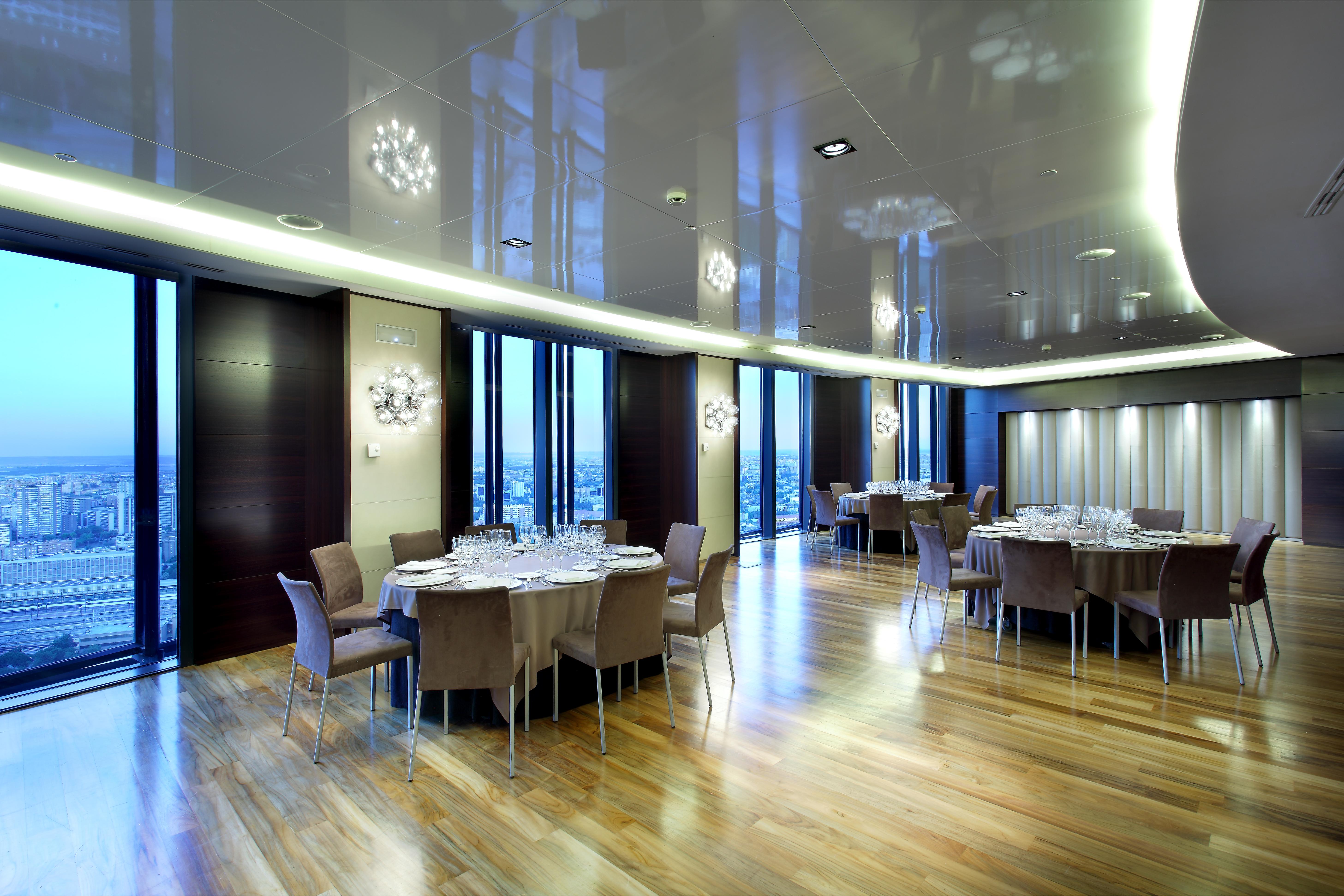 Eurostars Madrid Tower Hotel Exterior photo The photo depicts a modern dining room or banquet hall with large windows that provide a view of the outside. The room features elegant wooden flooring and contemporary furniture, including round tables set with plates, glasses, and cutlery. Various 