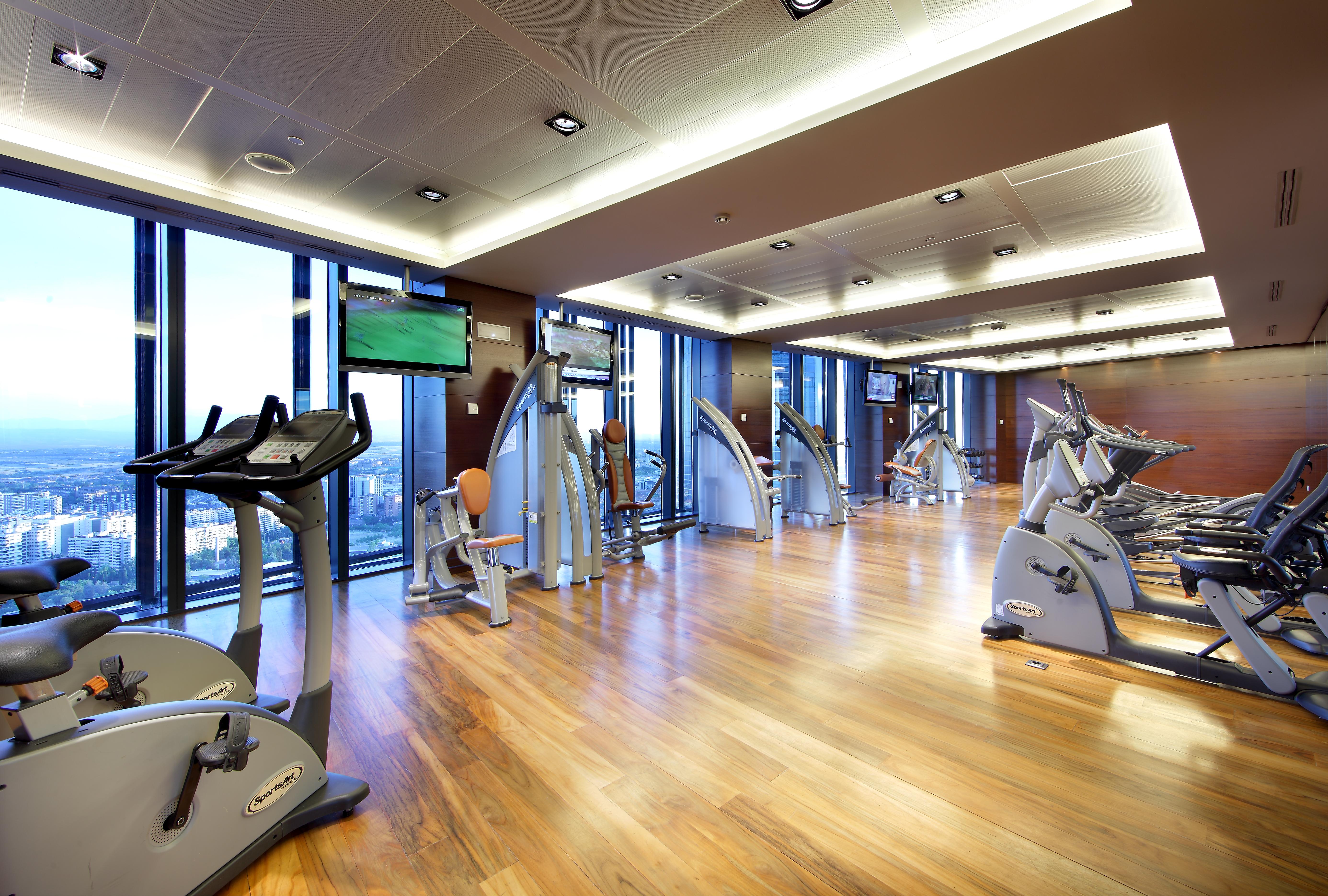 Eurostars Madrid Tower Hotel Exterior photo The photo shows a modern gym or fitness center. It features large windows that let in natural light, providing a view of the outside. The flooring is made of polished wood, giving the space a warm and inviting atmosphere. Various exercise machines ar