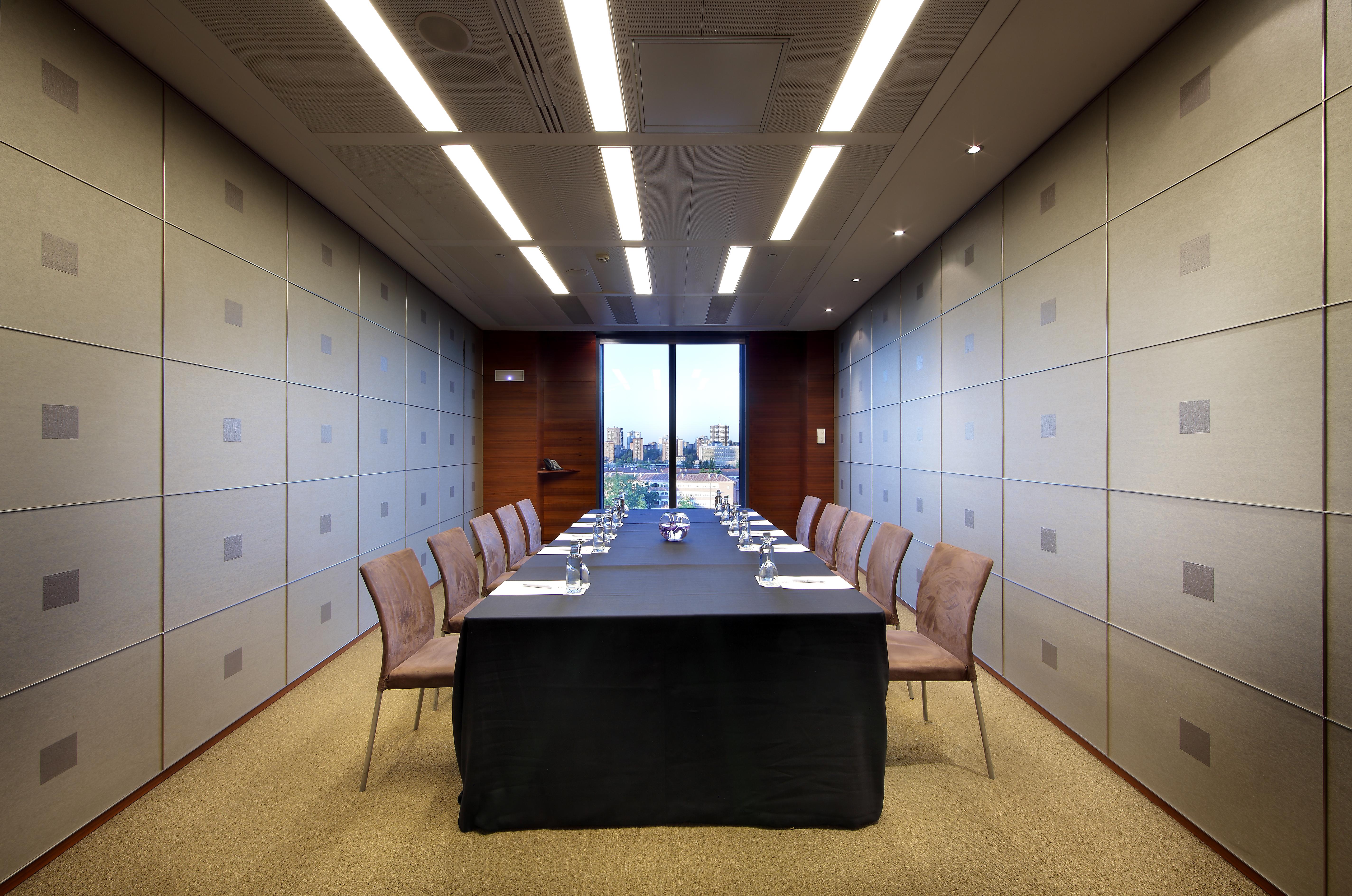 Eurostars Madrid Tower Hotel Exterior photo The photo shows a modern conference room. In the center, there is a long table covered with a black tablecloth. Surrounding the table are several chairs arranged neatly. The walls have a sleek design with light-colored panels, and overhead, there are