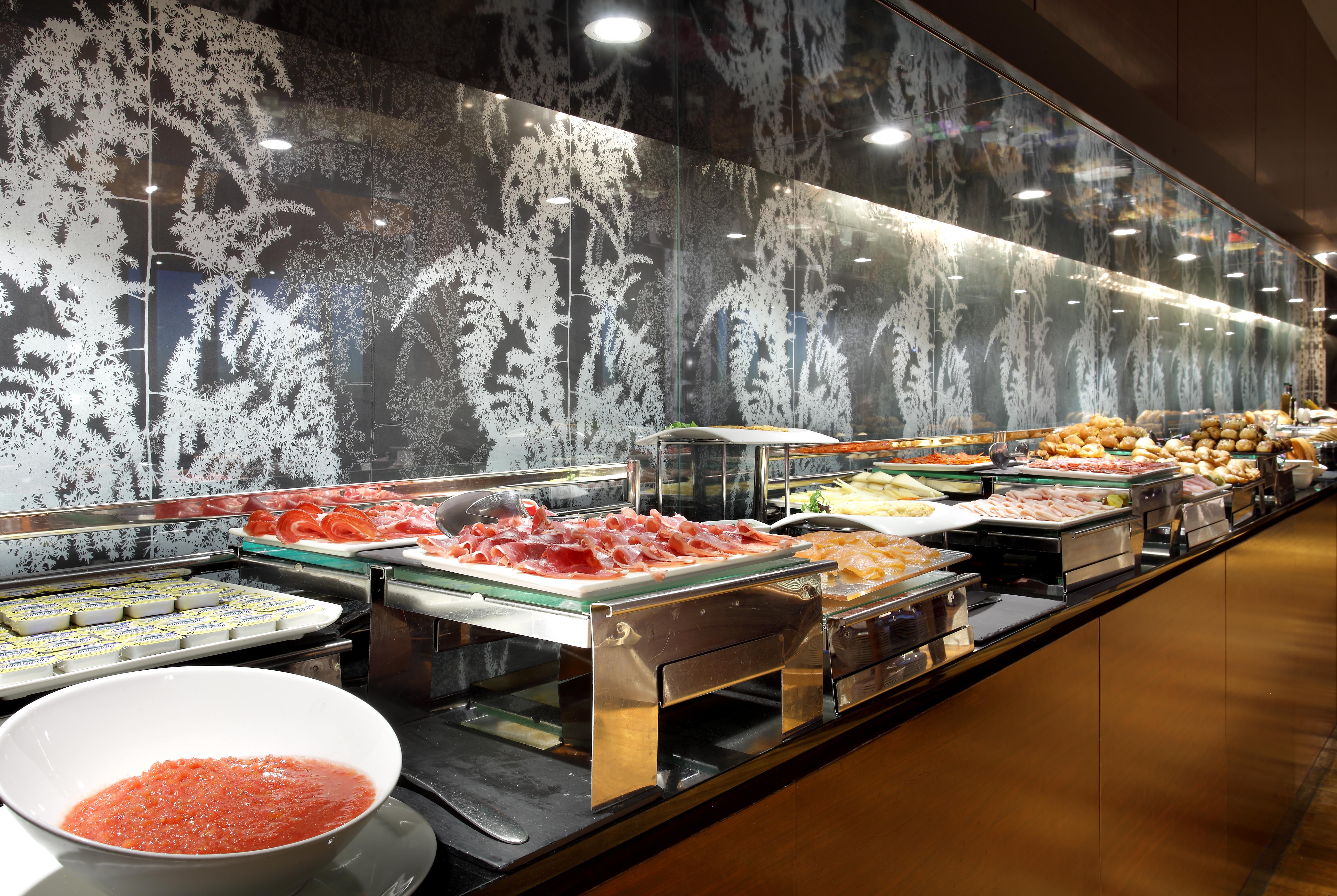 Eurostars Madrid Tower Hotel Exterior photo The photo shows a buffet setup featuring a variety of food items. There are multiple trays and containers displaying an assortment of dishes, including salads, meats, and other prepared foods. A large bowl of sauce or dressing is also visible in fron