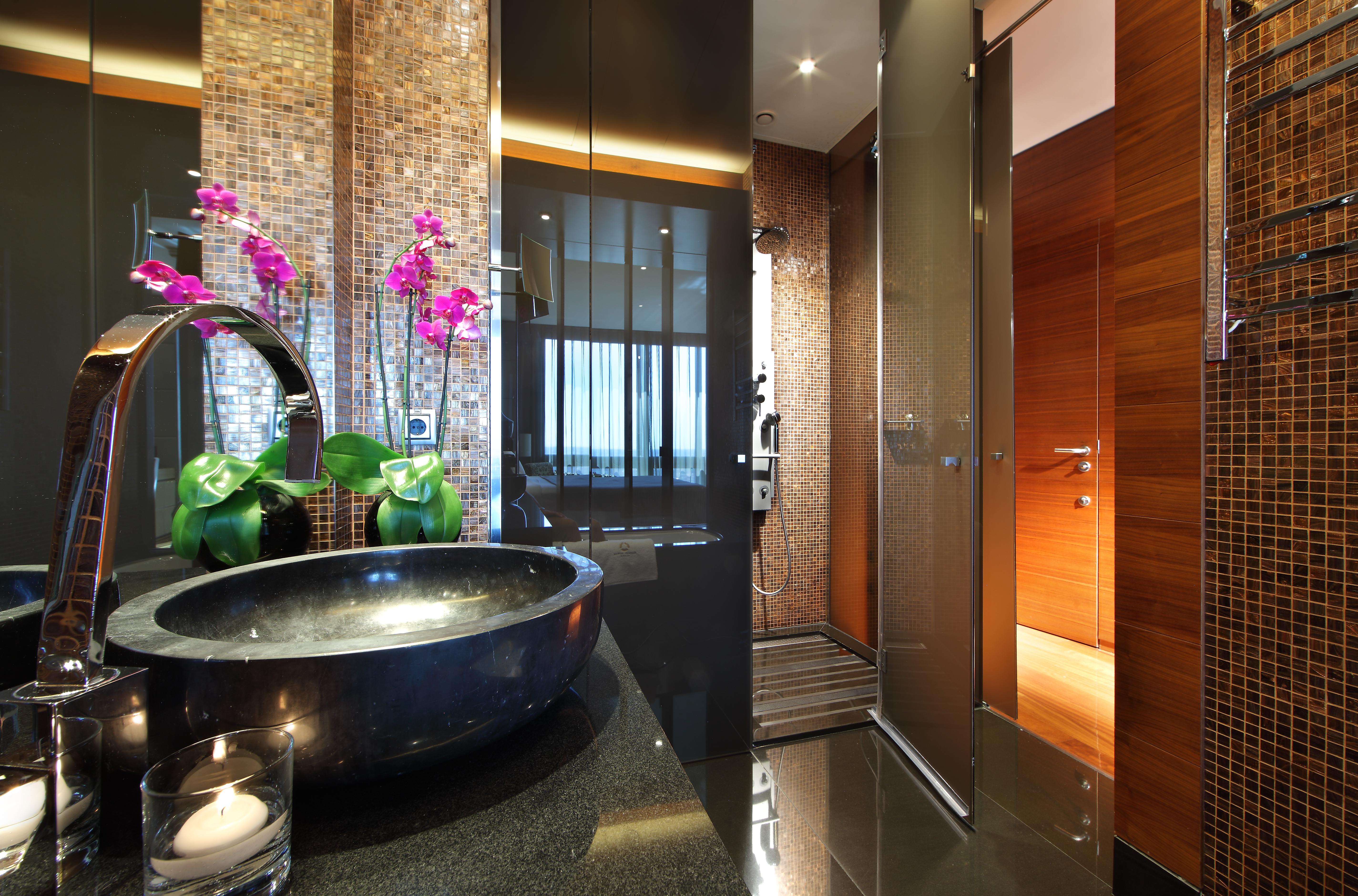 Eurostars Madrid Tower Hotel Exterior photo The photo shows a modern and stylish bathroom. On the left, there is a sleek black basin set on a dark countertop, adorned with decorative elements such as a candle and potted green plants. To the side, there are elegant pink orchids adding a pop of 