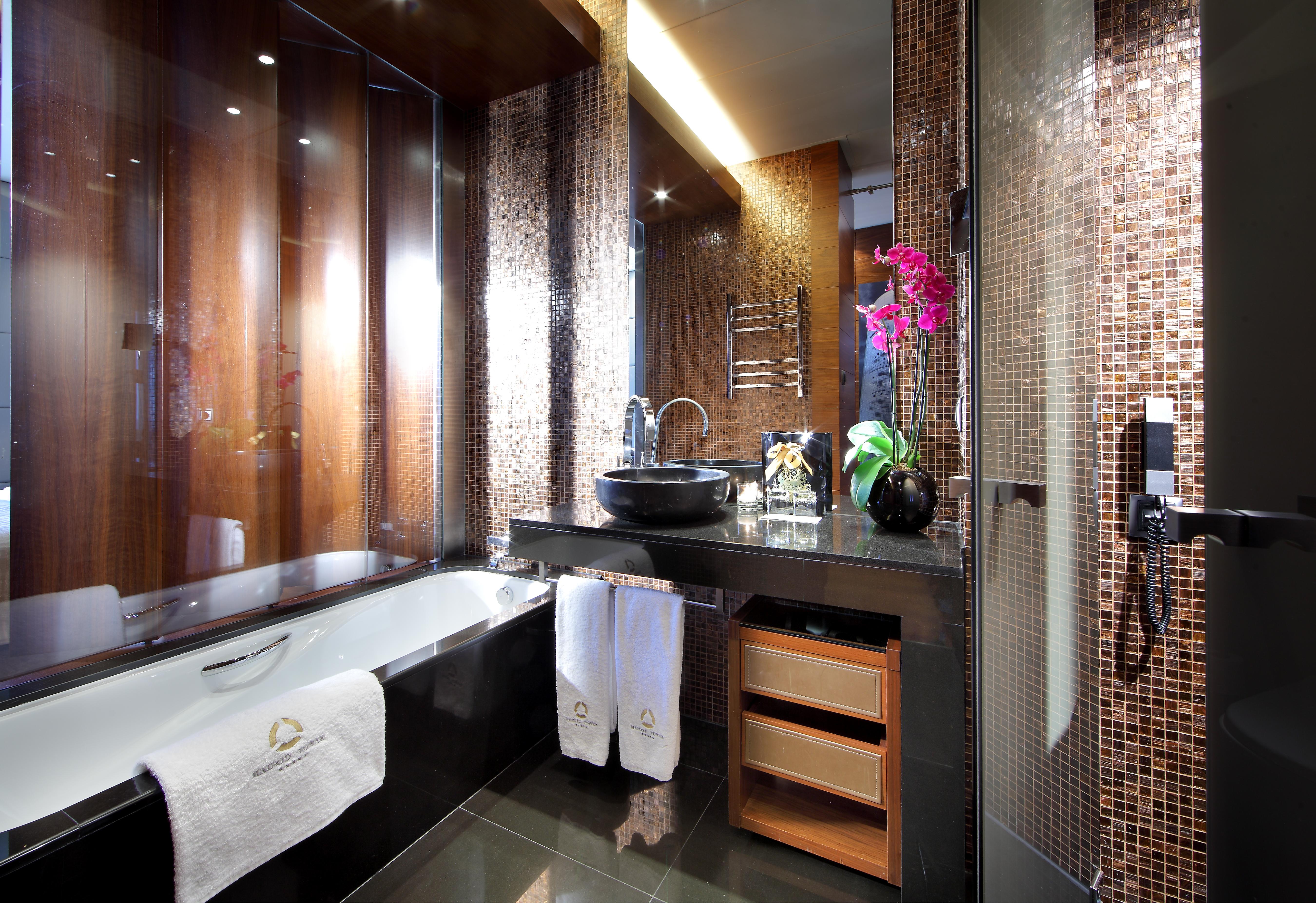 Eurostars Madrid Tower Hotel Exterior photo The photo shows a modern and elegantly designed bathroom. It features a luxurious bathtub on the left, accompanied by fluffy white towels. The sink area has a sleek black countertop with an artistic bowl sink, and there are various decorative element