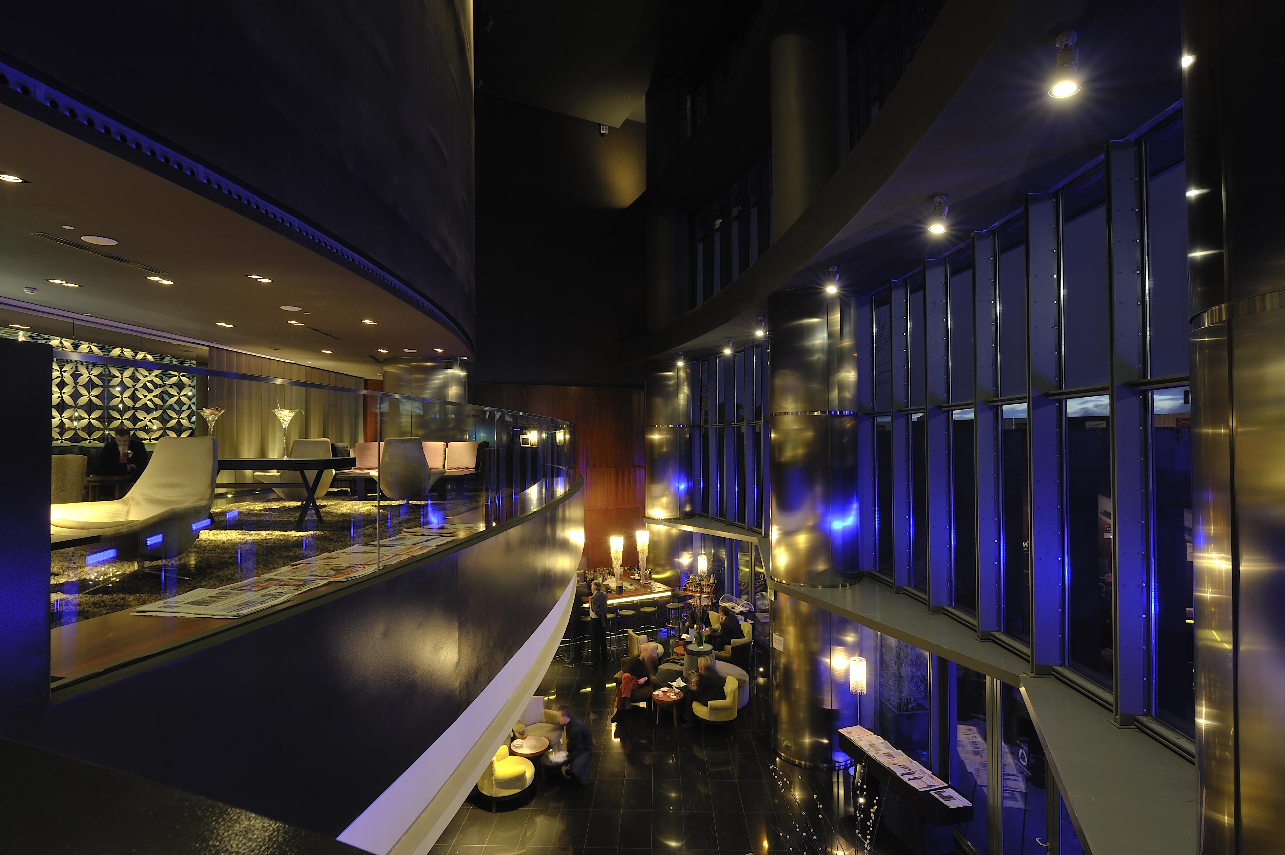 Eurostars Madrid Tower Hotel Exterior photo The photo depicts a modern and stylish interior space, likely a hotel lobby or lounge area. The design features smooth lines and a sleek aesthetic with a predominantly dark color palette complemented by subtle lighting. 

To the left, there are plush