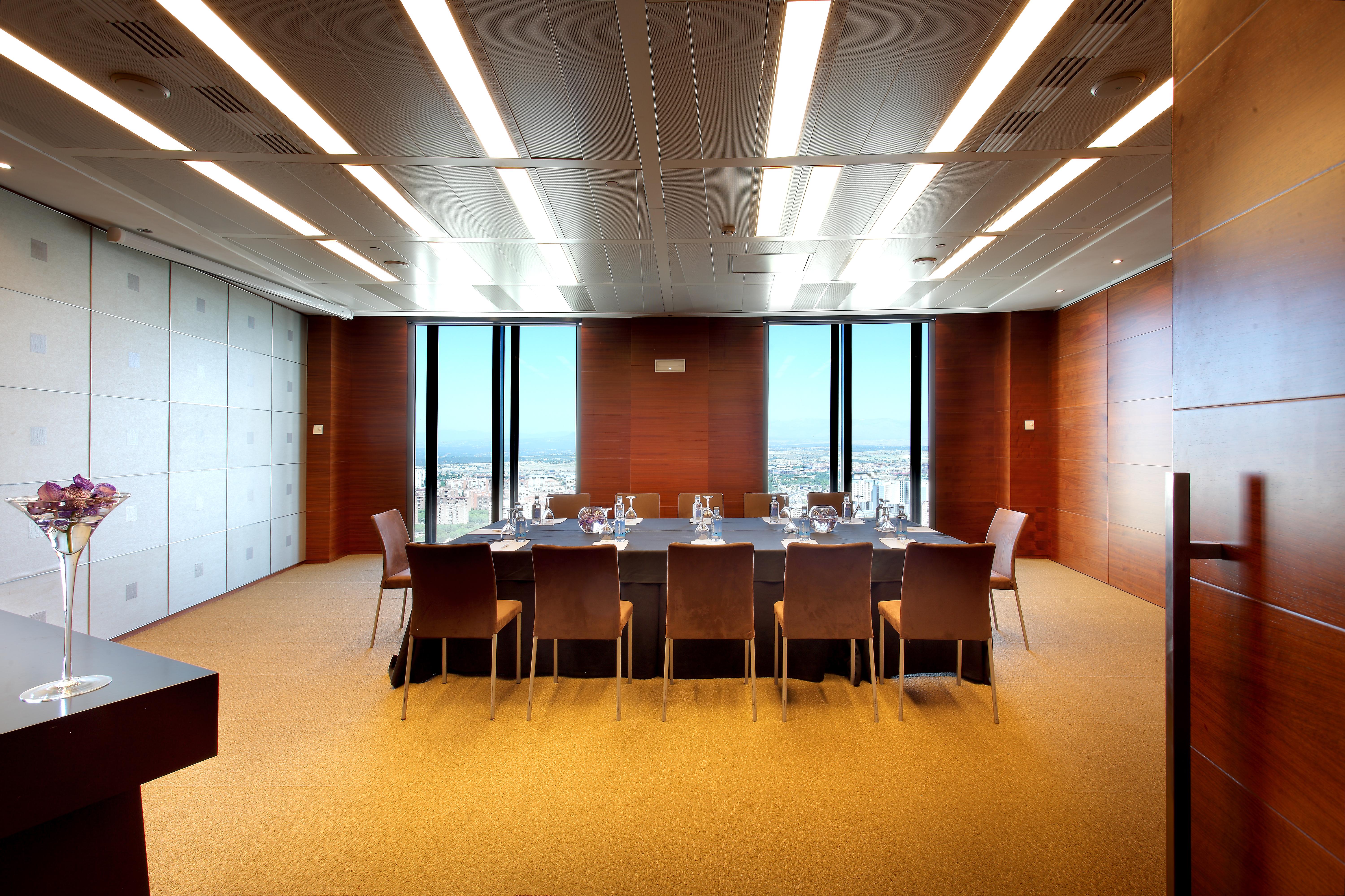 Eurostars Madrid Tower Hotel Exterior photo The photo shows a modern conference room or meeting space. It features a large rectangular table surrounded by several leather chairs. The room has wooden paneling and large windows that let in natural light, providing a view of the outside landscape