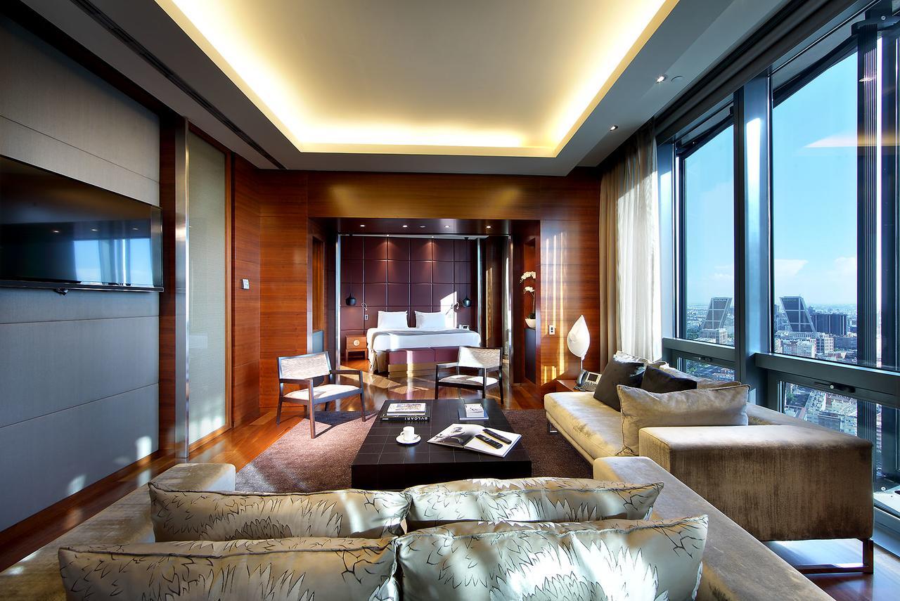 Eurostars Madrid Tower Hotel Exterior photo The photo shows a luxurious hotel room or suite with a modern design. It features large windows that offer a view of the outside, letting in plenty of natural light. The interior has warm wooden accents on the walls and sophisticated lighting through