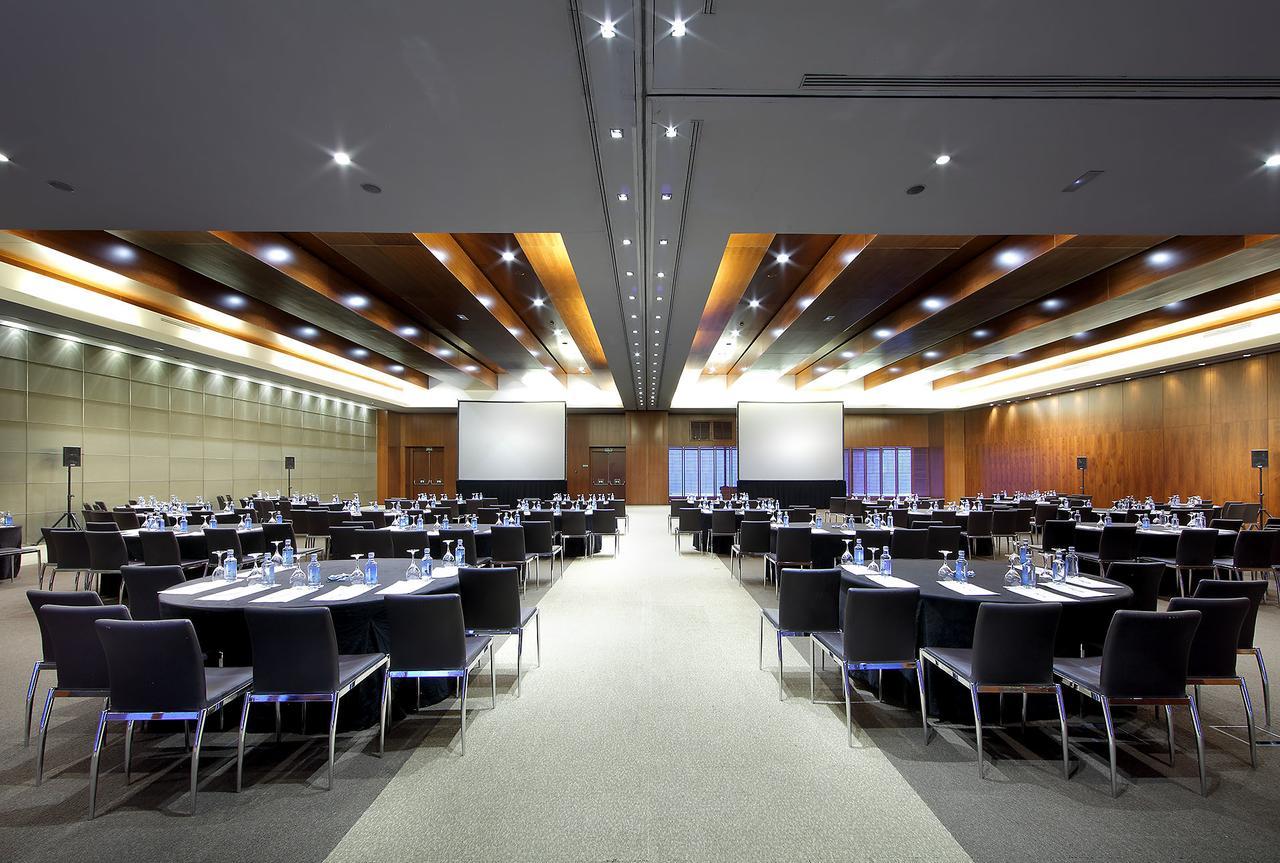 Eurostars Madrid Tower Hotel Exterior photo The photo shows a large conference or meeting room. It features multiple round tables set with chairs arranged around them, indicating that it is prepared for a formal gathering or event. Each table has water bottles and possibly notepads, suggesting