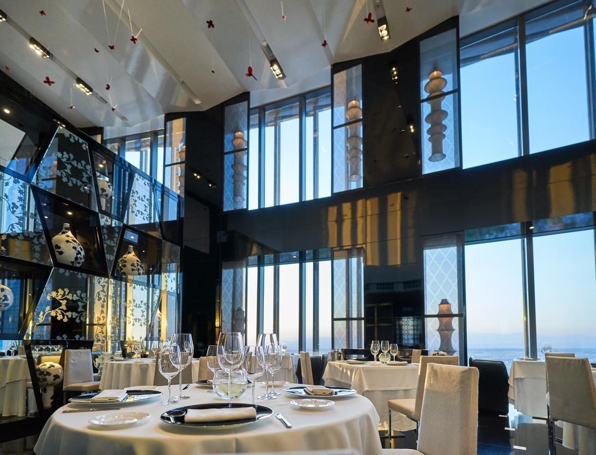 Eurostars Madrid Tower Hotel Exterior photo The photo shows an elegant restaurant interior featuring a modern design. The space has large windows that provide a view of the outside, allowing natural light to fill the room. The decor includes artistic elements, such as sculptures and decorative