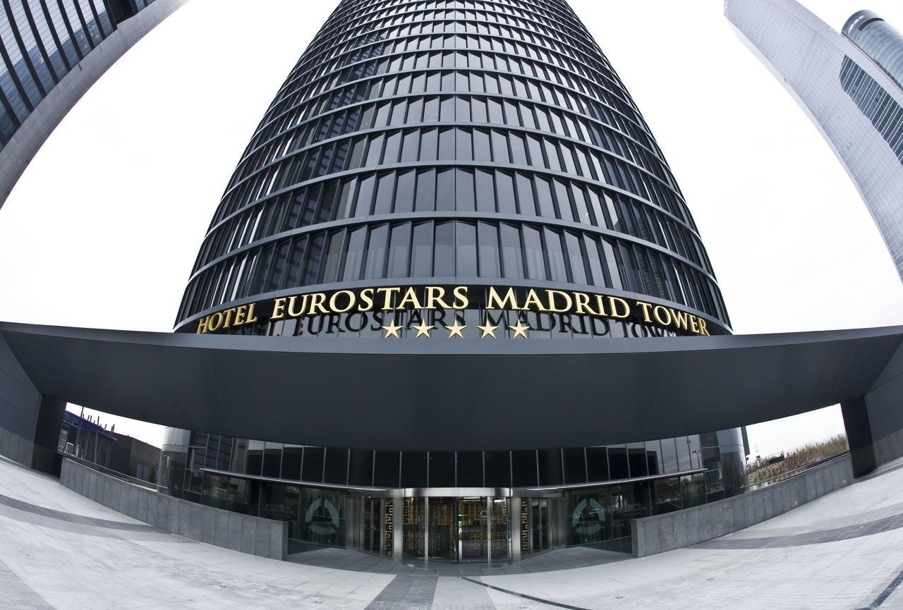 Eurostars Madrid Tower Hotel Exterior photo The photo shows a tall, modern glass building that serves as the Eurostars Madrid Tower Hotel. The building features a sleek, curved design with a prominent entrance. Above the entrance, the hotel's name is displayed in large golden letters, indicati