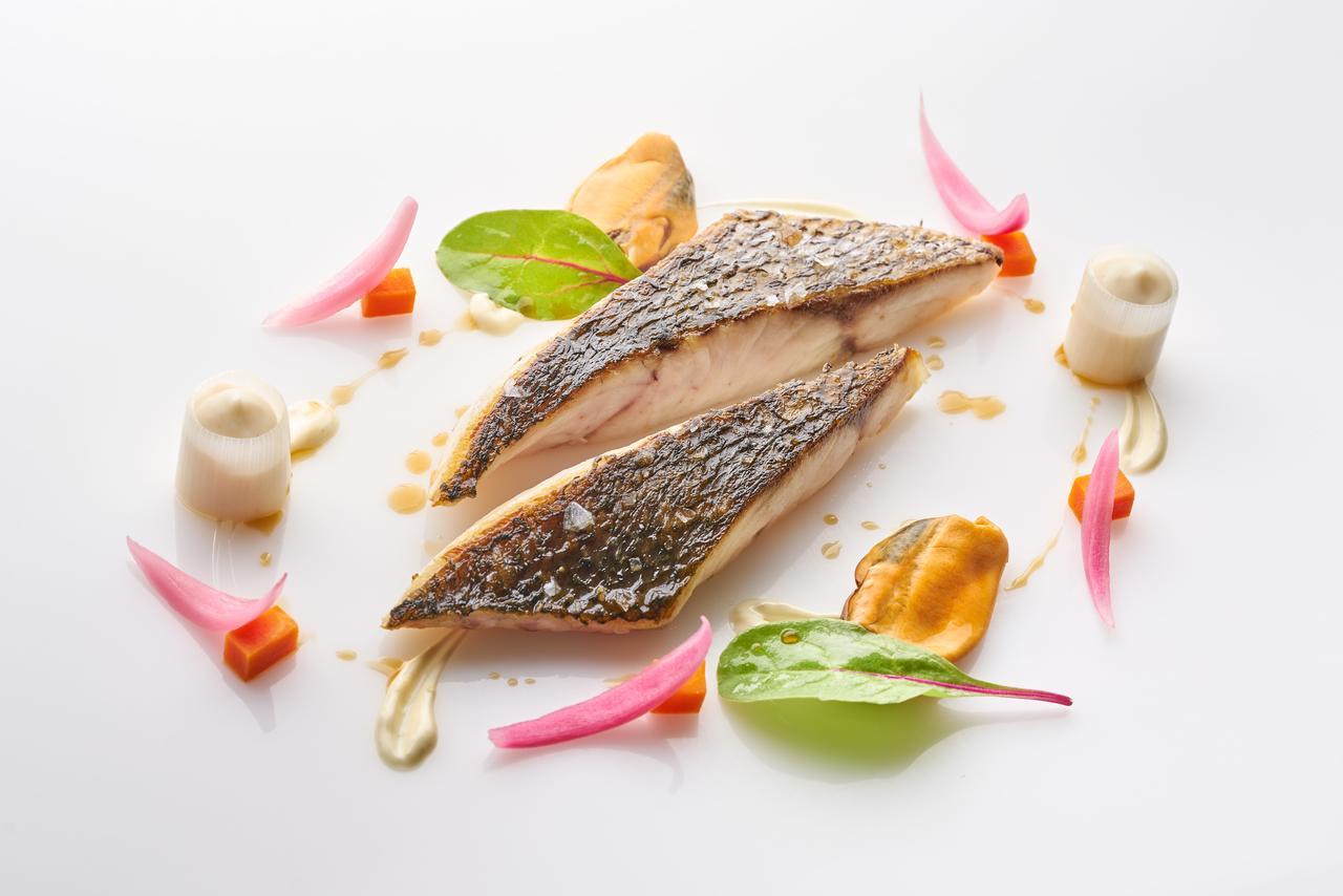 Eurostars Madrid Tower Hotel Exterior photo The image depicts a beautifully plated dish featuring two pieces of fish fillet, likely a type of white fish, arranged artfully on a white plate. The fish has a crispy skin and is cooked to a tender texture. Surrounding the fish are various garnishes