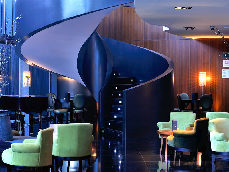 Eurostars Madrid Tower Hotel Exterior photo The photo depicts a stylish and modern interior, likely of a bar or lounge. The focal point is a unique spiral staircase that has a sleek, flowing design, leading to another level. The surrounding area features a combination of dark wood panels and g