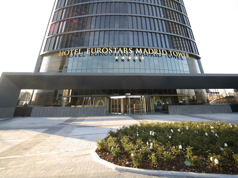 Eurostars Madrid Tower Hotel Exterior photo The photo shows the exterior of the Eurostars Madrid Tower Hotel, which is a modern, high-rise building. The hotel features a sleek glass facade and has "HOTEL EUROSTARS MADRID TOWER" prominently displayed in gold lettering above the entrance. The ar